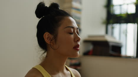 Young-asian-woman-meditate-alone-in-her-house,-close-up-of-female-focusing-on-breath-and-sharpening-the-mind-in-full-concentration-practice-portrait