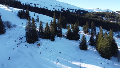 Low-overhead-aerial-clip-of-people-skiing-on-a-mountain-slope-at-Vitosha-ski-resort-near-Sofia,-Bulgaria-with-coniferous-forests-and-snow-covered-peaks-in-the-background