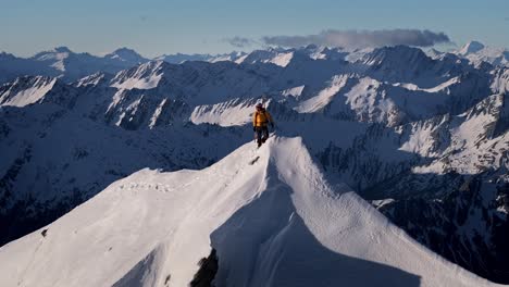 A-climber-stands-atop-a-Snowy-Mountain-in-the-wild-reaches-of-nature-with-huge-mountains-and-giant-valleys-in-the-background
