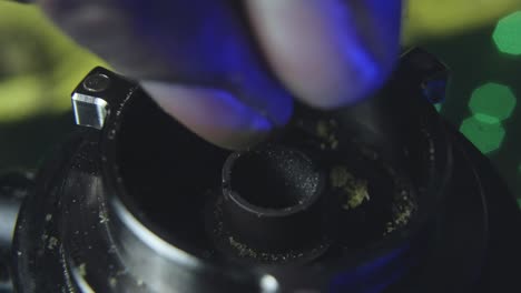 close-up-of-a-black-mans-hand-as-he-slowly-breaks-up-marijuana-bud-into-the-bowl-of-a-vaporizer-preparing-to-smoke-the-pot
