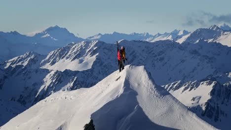 A-climber-stands-atop-a-Snowy-Mountain-in-wild-nature-with-huge-mountains-and-giant-valleys-in-the-background