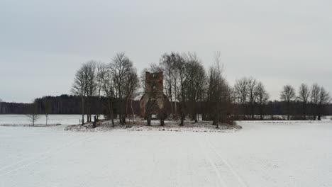 Low-aerial-approach-toward-abandoned-church-bell-tower-ruins,-winter-landscape