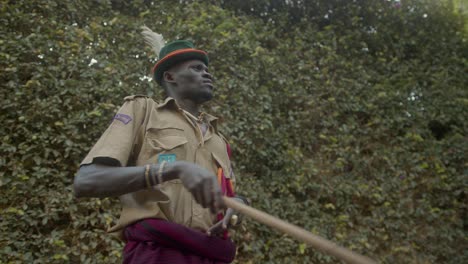 Afrikanischer-Krieger-Des-Karamojong-Stammes-In-Uniform-Mit-Holzstab,-Der-Mit-Dem-Finger-Im-Freien-In-Uganda-Zeigt