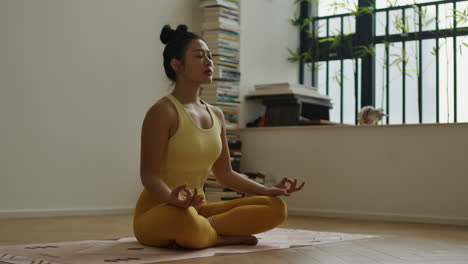Asiatic-woman-practicing-meditation-sitting-crossleg-in-her-home,-doing-mind-yoga-developing-concentration,-oriental-spiritual-practice