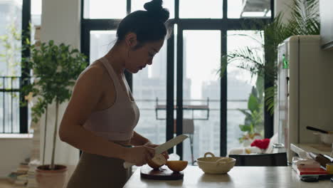 Asiatische-Frau-Schneidet-In-Zeitlupe-Birnenfrüchte-In-Ihrem-Modernen-Küchenapartment-Mit-Skyline-Stadtbild-Und-Blick-Aus-Dem-Fenster-Auf-Die-Moderne-Stadt