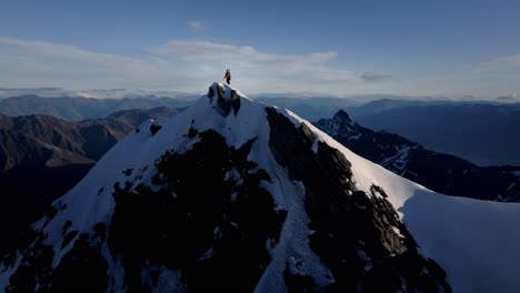 Ein-Majestätischer-Kletterer-Steht-Auf-Einem-Schneebedeckten-Berg-In-Der-Wilden-Natur-Mit-Riesigen-Bergen-Und-Riesigen-Tälern-Im-Hintergrund