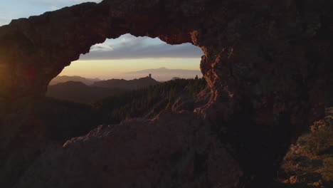 Cinematic-shot-going-through-the-window-of-Roque-Nublo-in-reverse-during-sunset