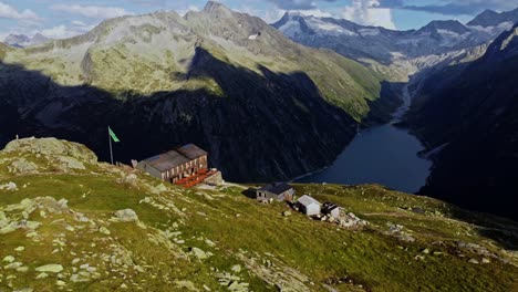 Orbit-drone-shot-beautiful-scenic-view-of-European-hut-named-"Olpererhütte"-in-Austrian-Alps-in-summer-with-the-Schlegeis-Stausee-below