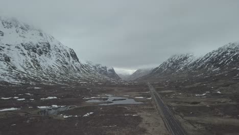 Aerial-backwards-shot-of-mountain-road-with-traffic-during-snowy-winter-day-in-Scottish-highlands