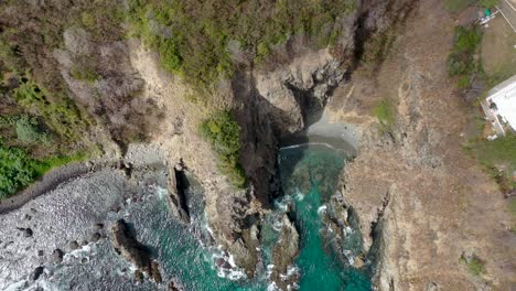 Drone-view-of-water-hitting-rock-on-Fernando-de-Noranha-Island,-Brazil,-paradise,-sea