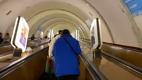 Gente-Tomando-Una-Escalera-Mecánica-Desde-Una-Estación-Subterránea-De-Metro-En-La-Capital-De-Kiev,-Ucrania,-Transporte-Rápido-Alrededor-De-Una-Ciudad,-Toma-De-4k