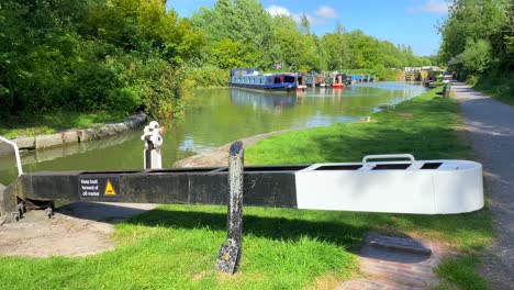 Nice-summer-day-on-the-Kennet-and-Avon-Canal-with-colourful-boats-in-Devizes-England,-pirate-flag,-sunny-weather-with-forest-trees-and-green-nature,-4K-shot