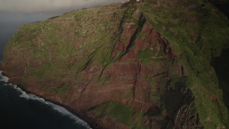 Vista-Aérea-Con-Drones-De-Una-Costa-Escarpada-De-Acantilados-Con-Exuberante-Vegetación,-Montañas-Y-Olas-Del-Océano-En-Tiempo-Nublado-En-Madeira