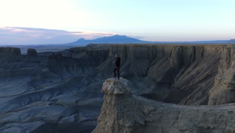 Drohne-Kreist-Um-Einen-Mann,-Der-Im-Morgengrauen-Auf-Einem-Felsvorsprung-Mit-Atemberaubender-Wüstenlandschaft-In-Utah-Steht