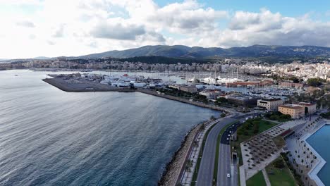 Aerial-flyover-coastal-road-to-Palma-City-with-beautiful-harbor-and-parking-yachts-and-sailing-boats-during-sunny-day