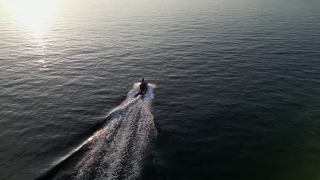 Drone-aerial-view-of-a-small-speedboat-cruising-on-the-ocean-during-sunset