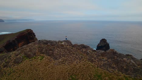 Drone-orbiting-around-a-person-at-the-edge-of-the-cliff-at-Madeira-by-the-ocean-coast-shore