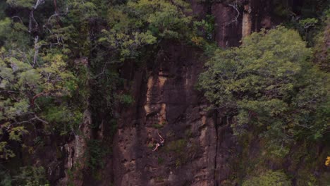 Climber-on-ropes-gives-thumbs-up-to-drone-before-rappelling-down-as-drone-backs-away-revealing-wide-landscape-view