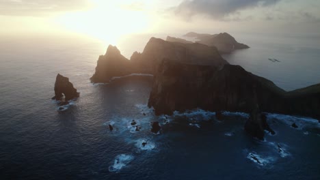 Drohne-Fliegt-Bei-Sonnenuntergang-über-Dem-Blauen-Ozean-An-Der-Zerklüfteten-Küste-Von-Madeira