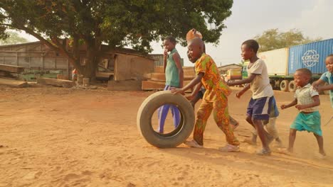 snow-motion-clip-of-a-group-young-African-children-playing-with-a-rubber-Tyre-in-the-dusty-field-near-a-tree,-children-running-around-and-having-fun
