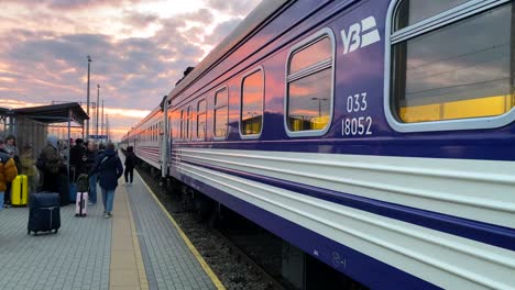 Ukrainian-Railways-Ukrzaliznycia-train-with-beautiful-pink-sunrise-sky-at-the-Chelm-train-station-in-Poland,-Ukrainian-refugees-waiting-to-board-early-morning-train-to-Kyiv-Ukraine,-4K-tilting-up