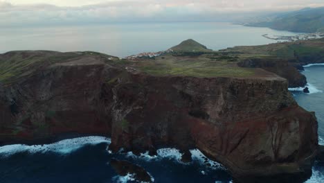Drone-flying-over-the-sea-by-the-coast-at-Ponta-Do-Rosto,-Madeira-while-scenery-landscape-visible-in-the-background-with-waves-and-mountains-at-Madeira