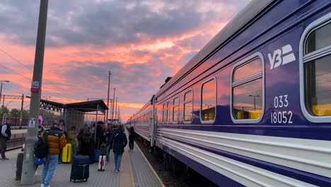Ukrainian-Railways-Ukrzaliznycia-train-with-beautiful-pink-sunrise-sky-at-the-Chelm-train-station-in-Poland,-Ukrainian-refugees-waiting-to-board-early-morning-train-to-Kyiv,-4K-shot