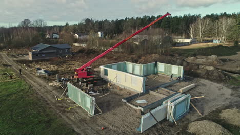 Construction-site-with-workers-and-crane-assembling-prefabricated-house-modules,-aerial-view