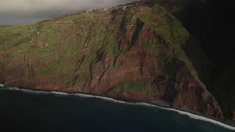 Aerial-view-with-drone-of-a-rugged-cliff-coastline-with-lush-greenery-mountain-and-ocean-waves-in-cloudy-weather-in-Madeira