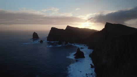 Drone-flying-over-the-blue-ocean-during-sunset-at-the-coastal-rugged-shore-at-Madeira