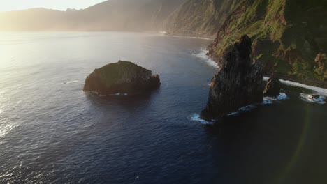 Aerial-view-with-drone-of-rugged-cliffs-and-isolated-rocks-in-the-ocean-during-golden-hour