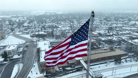Aerial-close-up-of-American-flag-waving-over-snowy-suburban-landscape