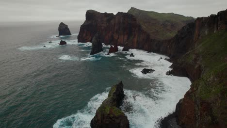 Drone-flying-over-the-wavy-sea-while-rugged-coastal-cliffs-are-visible-in-the-background