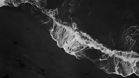 Aerial-from-the-top-view-of-a-beach-with-waves-hitting-up-the-sand,-black-and-white-shot-of-the-beach