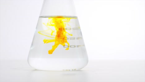 Close-up-shot-of-the-titration-process,-yellow-die-drop-being-mixed-in-colorless-fluid-in-the-glass-beaker