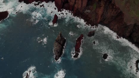Aerial-top-shot-with-a-drone-at-Ponta-Do-Rosto-over-the-sea-about-rugged-cliffs-and-rocks,-waves,-and-mountain-ridges