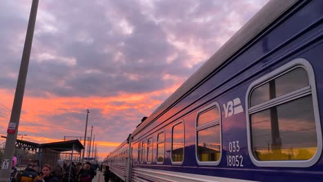 Ukrainian-Railways-Ukrzaliznycia-train-with-beautiful-pink-sunrise-sky-at-the-Chelm-train-station-in-Poland,-Ukrainian-refugees-waiting-to-board-early-morning-train-to-Kyiv-Ukraine,-4K-tilting-down