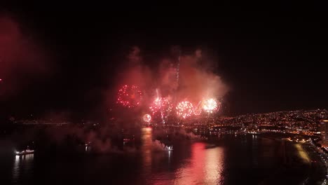 Dolly-out-flyover-of-the-city-of-Valparaiso-Chile-at-night-with-ships-on-the-coast---fireworks-at-the-New-Year's-Eve-show