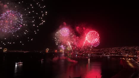 Dolly-in-bird's-eye-view-of-ships-launching-fireworks-in-a-coordinated-manner-in-Valparaiso-at-night,-Chile