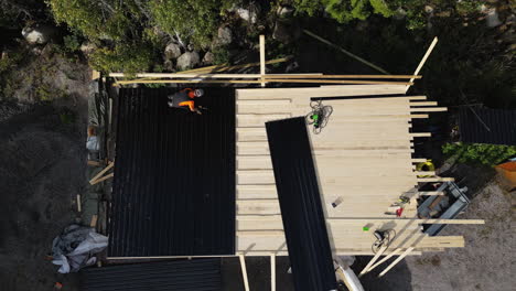 Aerial-view-of-a-construction-worker-roofing-a-cabin-among-trees-in-daylight