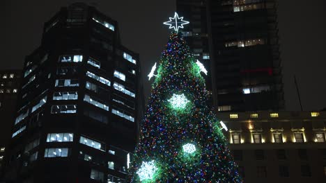 Vancouver-city-very-large-and-tall-christmas-tree-lit-up-and-glowing-surrounded-by-the-tall-lit-up-buildings-and-skyscrapers-at-on-a-winter-night-in-the-dark