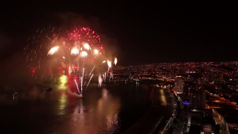 Aerial-view-establishing-Valparaiso-at-night-with-the-New-Year's-Eve-fireworks-display,-city-illuminated-by-lights-and-sparkles