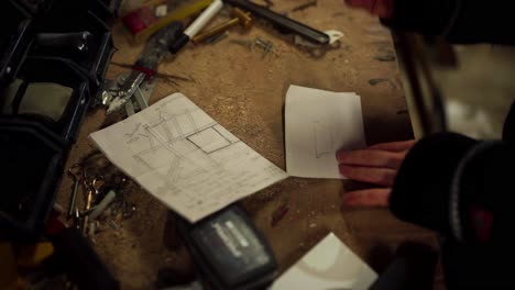 Man-Draws-On-Piece-Of-Paper-In-The-Wood-Workshop-Table