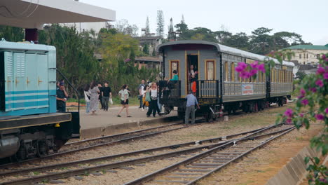 Estación-De-Tren-Da-Lat:-El-Antiguo-Tren-Locomotora-Viaja-Sobre-Las-Vías-Mientras-La-Gente-Entra-En-Un-Antiguo-Vagón-De-Tren,-Grupos-De-Turistas-Caminan-Por-La-Plataforma