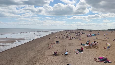 Crowds-of-happy-holidaymakers,-tourists-gather-on-the-beach-at-the-seaside-town-of-Skegness