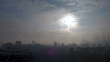 Frosty-rooftops-across-an-East-End-estate-are-enveloped-in-freezing-fog-as-the-sun-breaks-through-cloud-over-an-obscured-Canary-Wharf-financial-district