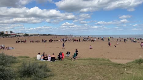 Crowds-of-happy-holidaymakers,-tourists-gather-on-the-beach-at-the-seaside-town-of-Skegness