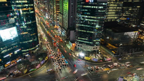 Gangnam-Main-Street-Night-Traffic-And-Towering-Office-Skyscrapers-in-Seoul---Aerial-Hyperlapse,-Cars-Crossing-Jammed-Crossroad---pull-back-zoom-out