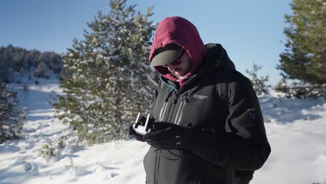 Young-male-drone-pilot-flying-his-drone-snow-covered-mountain-forest-winter