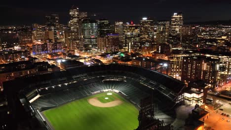 Aerial-Drone-Flyover-of-Coors-Field-Baseball-stadium-at-night-time-with-the-Denver,-Colorado-Skyline-in-the-background